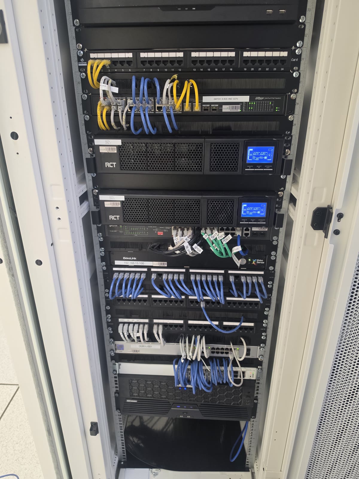 Front of an installed equipment cabinet with patch panels, network switches and UPS units